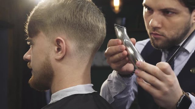 Cropped close up of a handsome professional barber working at his barbership using electrical clipper or trimmer styling hair of his male client service occuaption profession job worker masculine.