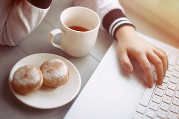 Laptop, hand, cup and plate with cookes on table