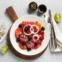 typical Spanish-style salad of red orange, onion and olives with capers and fresh raw olive oil and lime juice . Served on a stone white table. summer healthy snack or light lunch, copy space