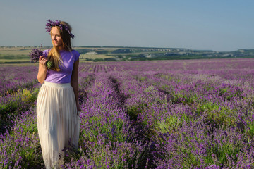 Fototapeta na wymiar Charming girl in a hat and a light dress posing in a lavender field at sunset