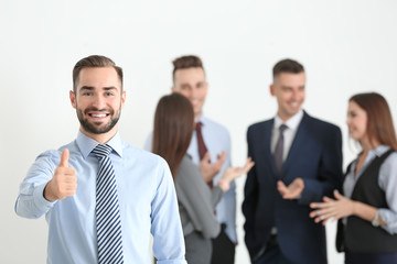 Young businessman showing thumb-up gesture and his team on background