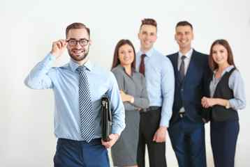 Young businessman with briefcase and his coworkers on background
