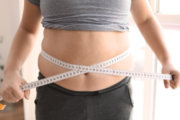 Overweight boy measuring his waist at home, closeup