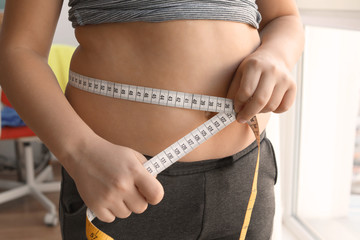 Overweight boy measuring his waist at home, closeup