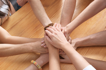 People putting hands together at wooden table as symbol of unity