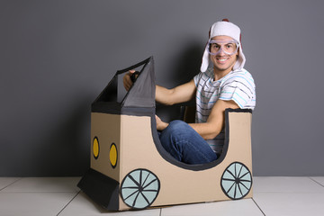 Young woman playing with cardboard auto near grey wall. Concept of buying new car