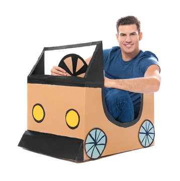 Young man playing with cardboard auto against white background. Concept of buying new car