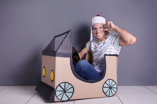 Young woman playing with cardboard auto near grey wall. Concept of buying new car