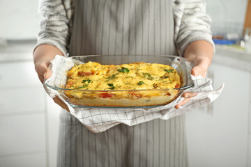 Woman holding glass baking dish with delicious casserole indoors, closeup. Fresh from oven
