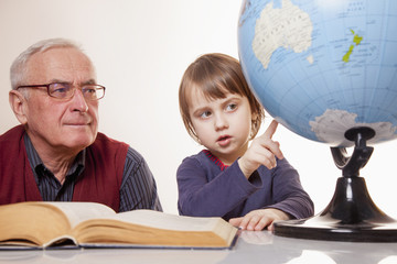 Global travel and geography concept. Portrait of happy grandfather and granddaughter looking at globe and dream of a trip.