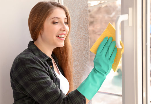 Young woman cleaning window indoors