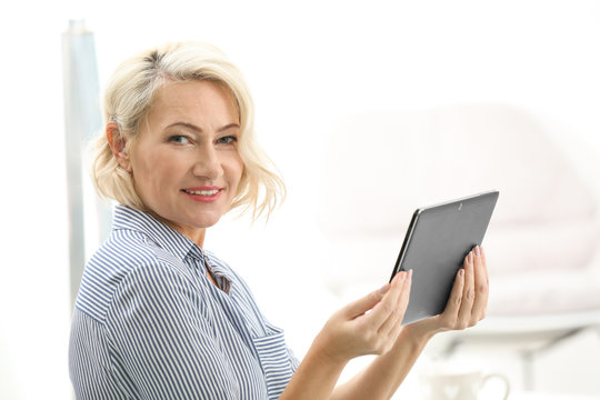 Mature woman with hearing aid using tablet computer indoors
