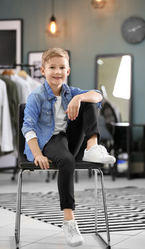 Cute boy in denim shirt sitting on chair, indoors