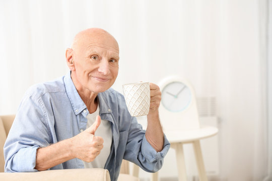 Hearing impaired man with cup of tea showing thumb up gesture at home