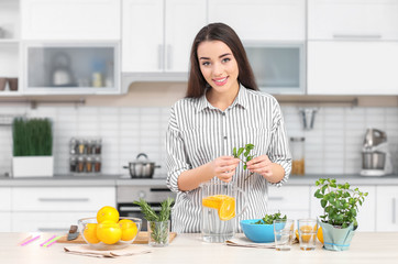 Young woman preparing tasty lemonade in kitchen