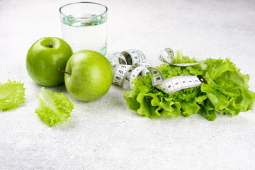 Healthy eating. Green apple, lettuce salad, glass of water, measuring tape. Dieting, slimming, weight loss and meal planning concept