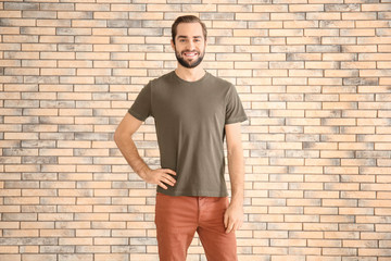 Young man in stylish t-shirt against brick wall. Mockup for design