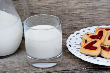 Glass of milk with heart cookies in a plate on table