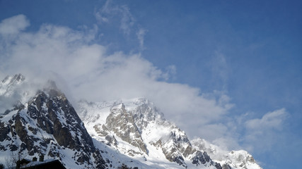 Fototapeta na wymiar Mountains covered with snow, blue sky with clouds and winter forest near Mont Blanc Alpes, Italy