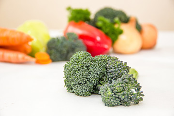 Different vegetables and fresh herbs on the white table. broccoli sprouts on the front. Orange carrot, onions and red pepper blurred on the background