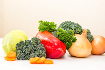 Different vegetables and fresh herbs with waterdrops on the white table. Orange slices of carrot and green broccoli sprouts, raw not-pealed onion, red sweet pepper in the center