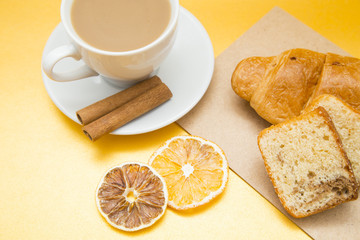 I love coffee concept. Coffee cup, croissant and sun dried orange on yellow background. Closeup