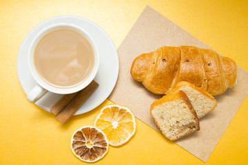 I love coffee concept. Coffee cup, croissant and sun dried orange on yellow background. Closeup and top view