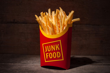 French fries in red paper packing with words JUNK FOOD on a wooden table