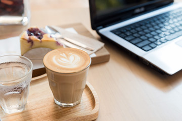 coffee cup latte art with cake and laptop computer on a wooden table in a coffee shop.