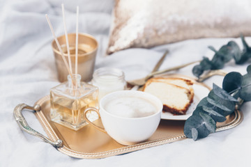 Gold tray with coffee and eucalyptus on clean white bedding. Good morning concept.