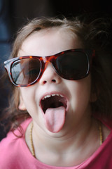 Little kid girl showing the tongue on dark background. © sharafmaksumov