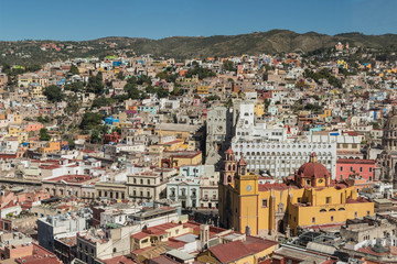 Looking down on a UNESCO Heritage Site-Guanajuato City, Mexico, from up on a hill, with a view of the Basilica, Guanajuato University, many other buildings, colorful houses and hills - 192049113