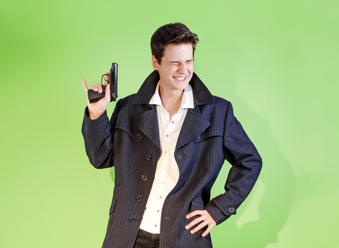 Young cheerful brunette in a dark coat. emotional portrait. image of a gangster with a gun. Desktop Wallpapers