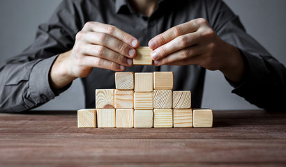 Businessman building a pyramid of wood blocks. Concept of business hierarchy and business strategy.