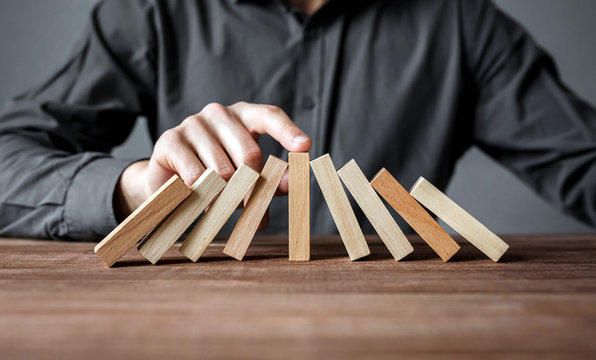 Businessman stopping domino effect with his finger. Security and insurance concept.