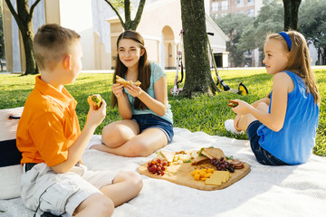 Smiling Caucasian brother and sisters eating food at picnic