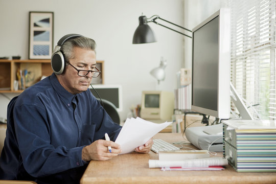 Hispanic businessman reading paperwork and listening to headphones
