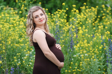 Naklejka na ściany i meble Pregnant happy woman in a flowering field outdoors