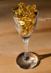 Yellow Omega 3 fish oil capsules in glass on wood background with shadows
