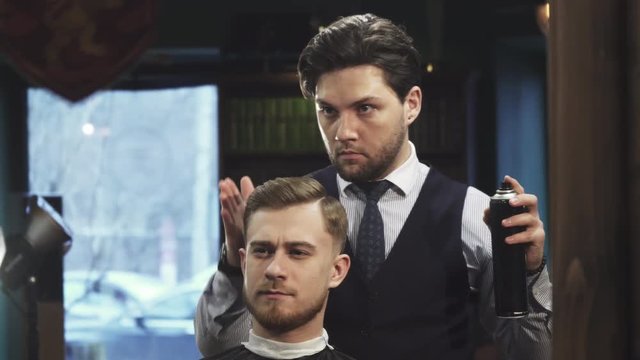 Young handsome professional barber working at his barbershop styling hair of his client profession occupation career job barbering consumerism service masculinity cutomer fashion men.