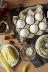 Preparation for baking. Eggs in a tray, oatmeal in a jar, spices, nuts, jam and butter. Gray linen napkin on kraft paper. Flat lay.