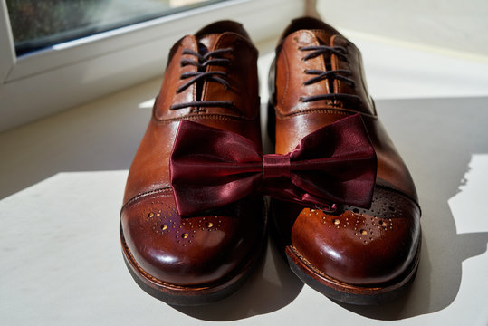 Close up of burgundy man bowtie on brown leather man shoes. Modern man accessories. Wedding details. Groom accessories. Men's casual outfits with shoes and bowtie