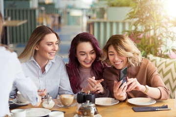 Young beautiful girls taking selfie photo at cafe or coffee shop. Happy women friends having fun, talking together and looking photos at mobile phone. Female friendship, communication concept