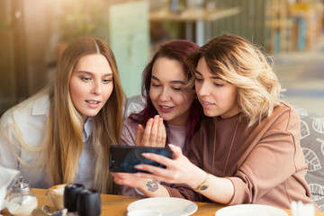 Young beautiful girls taking selfie photo at cafe or coffee shop. Happy women friends having fun, talking together and looking photos at mobile phone. Female friendship, communication concept