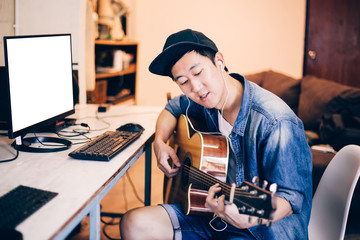 Young Asian man learning how to play guitar on computer monitor. Male guitarist watching online tutorial. Include clipping path on monitor
