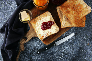 Toast bread with homemade strawberry jam and orange marmalade on rustic table served with butter...