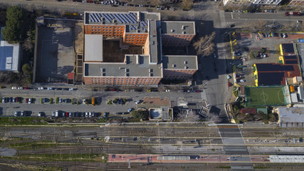  Perpendicular aerial view of a square orange building located in Rome, Italy. Around the building there are streets where there are parked cars and planted trees.