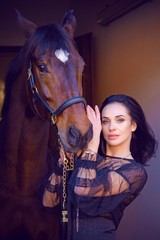 Fototapeta na wymiar Gorgeous stylishly dressed woman in dark lace boho style dress and gold jewelry with a thoroughbred horse. The concept of love human and animals, horses and rider lifestyle 