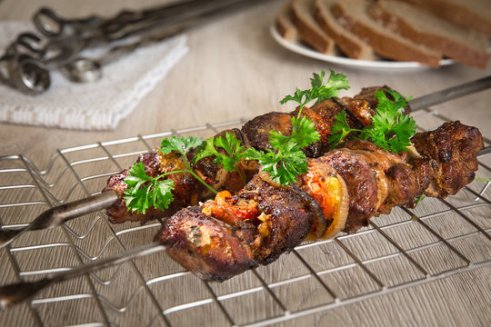 Kebabs on skewers. Roasted meat, tomatoes, pepper, parsley and onion on the white dish with vegetables on the wooden table.