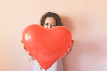 ​Beautiful curly young woman holding a heart shape air balloon on color background. Valentine's Day concept, symbol of love.